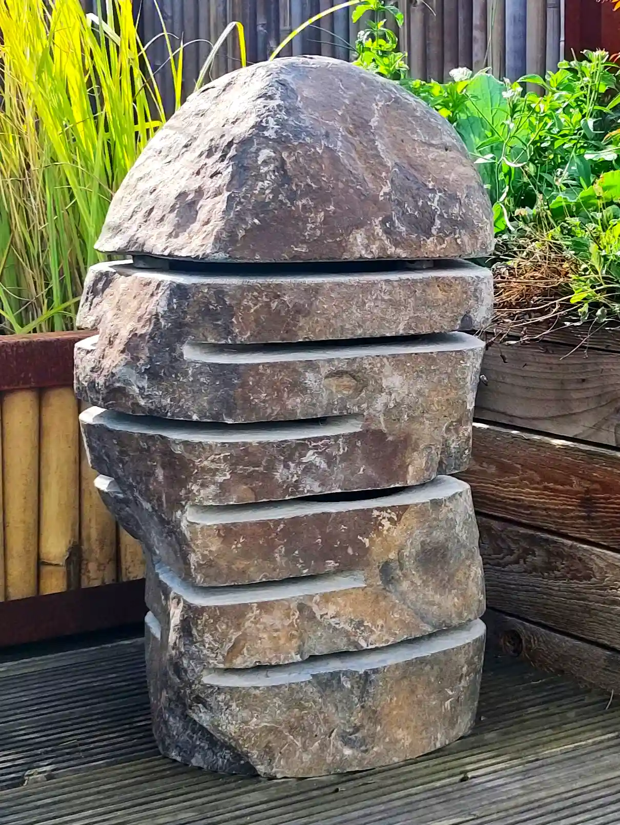Steinlampe mit warmen Licht neben Blumenbeet und Holzeinfassung im Garten.