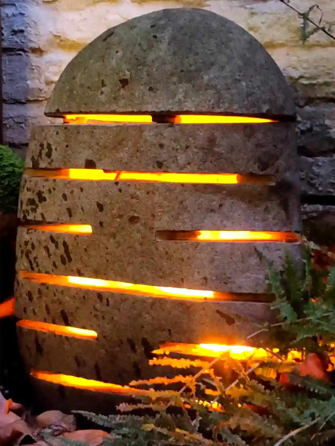 Steinlampe mit waagerechten Schlitzen und warmen Lichtschein im Garten bei Nacht.