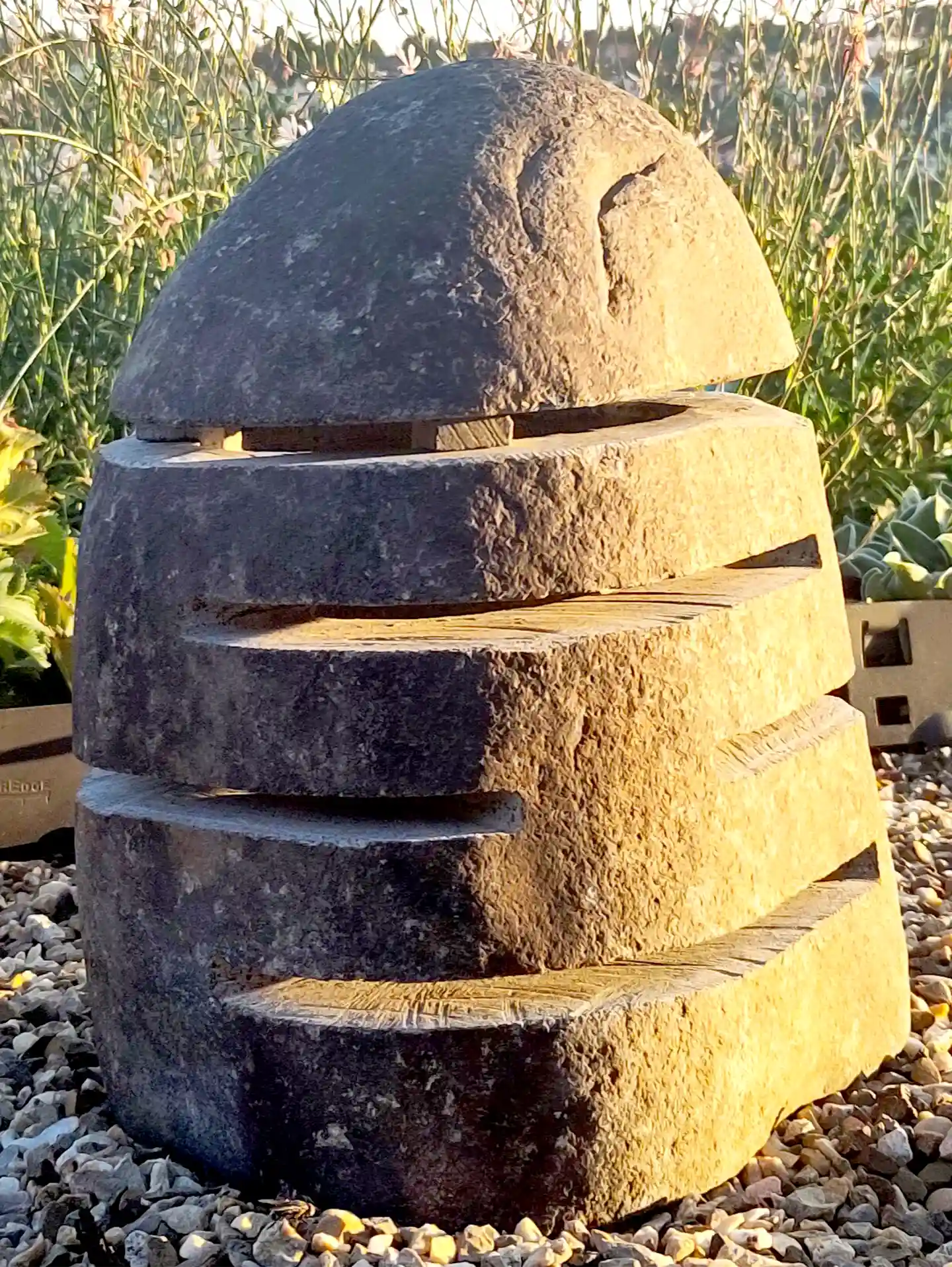 Steinlampe mit eingeschnittenen Lichtschnitzen aus Naturstein im Sonnenschein.